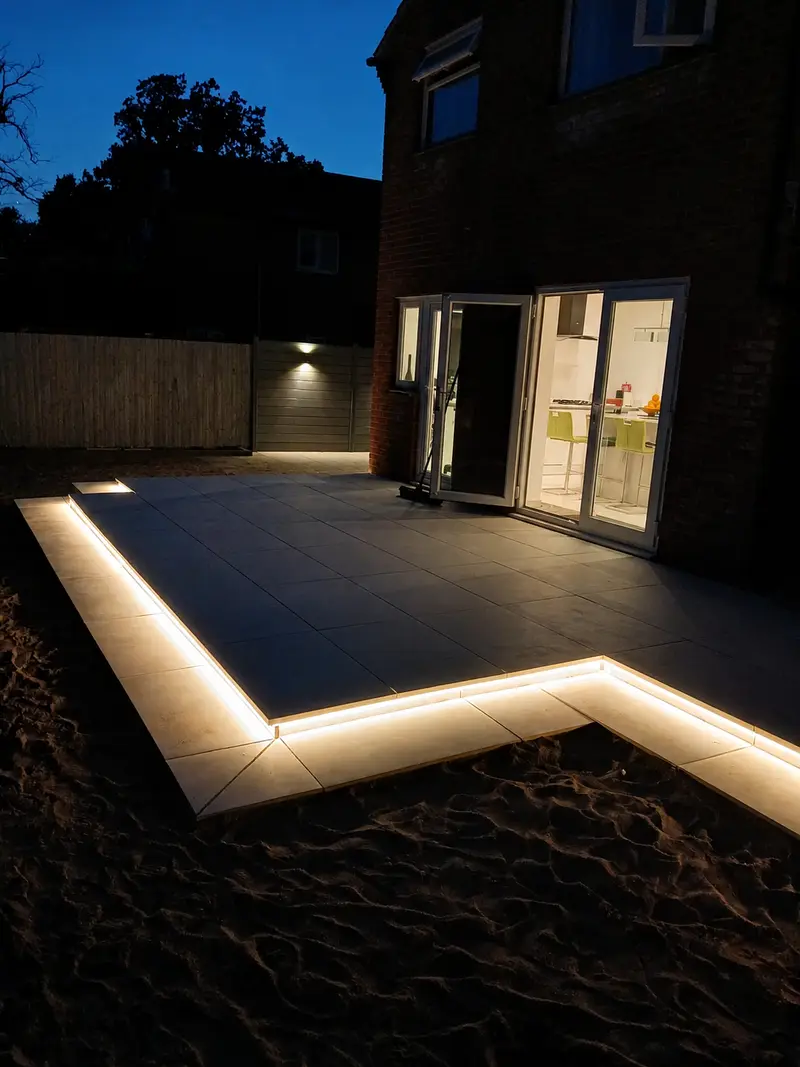 Dark porcelain patio at night with recessed LED strip border and open kitchen doors